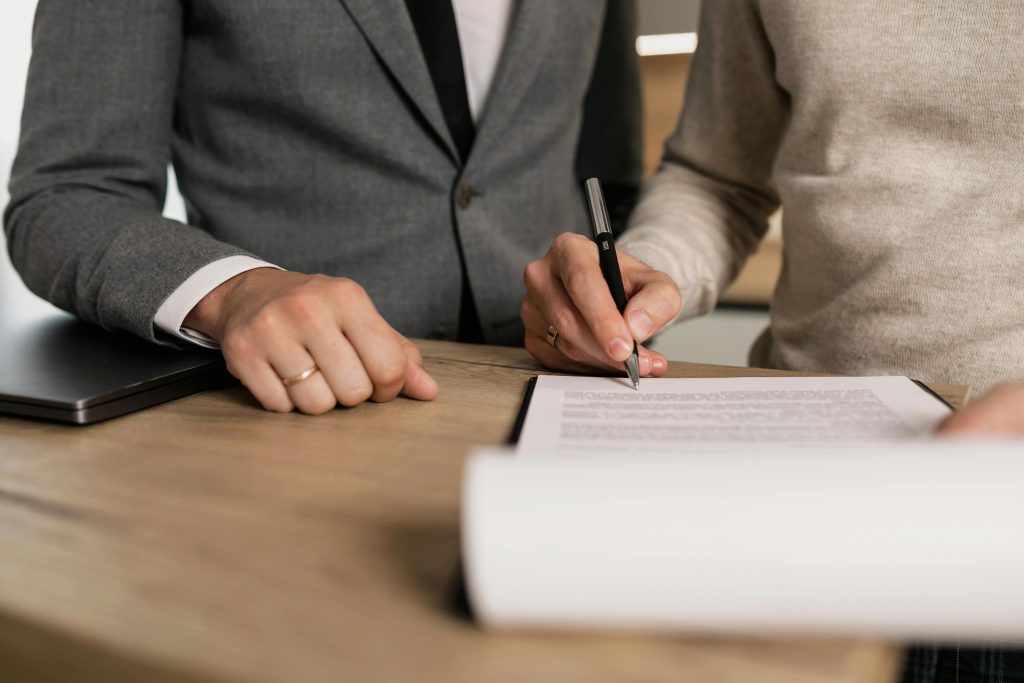 pexels-photo-7641842-7641842 Close-up of businessmen signing documents at a wooden table in an office.